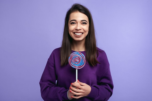 Hipster girl with big candy smiling over bright violet