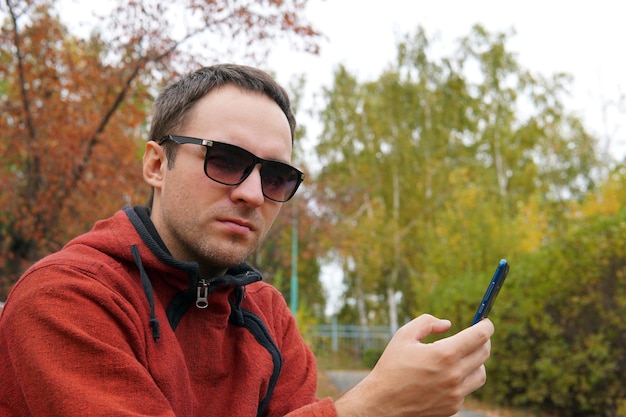 Hipster guy using smartphone device outdoor outdoor portrait of young cheerful man texting an sms message at social networks technology concept displeasure disaffection resentment frustration