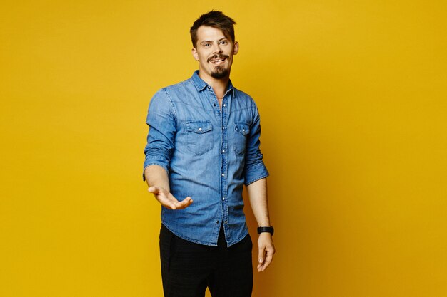 Hipster guy with beard and mustache raising one hand with a surprised gesture and looking aside posing