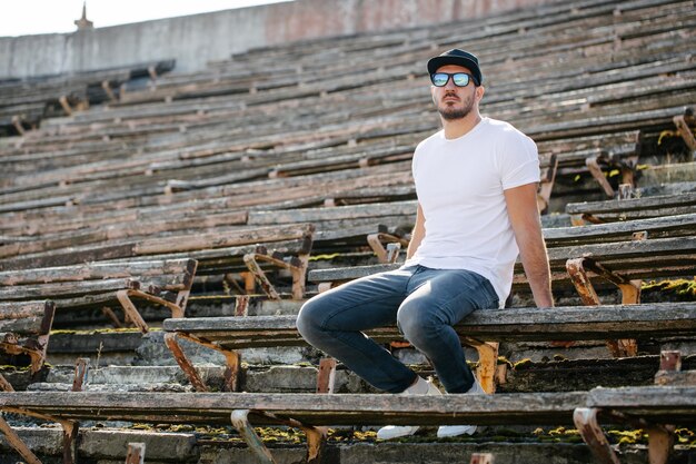 Hipster handsome male model with beard wearing white blank t-shirt and a baseball cap with space for your logo or design in casual urban style