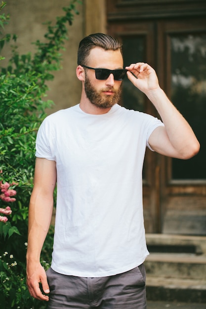 Фото Хипстерская красивая мужская модель с бородой в белой пустой футболке с местом для вашего логотипа или дизайна в повседневном городском стиле