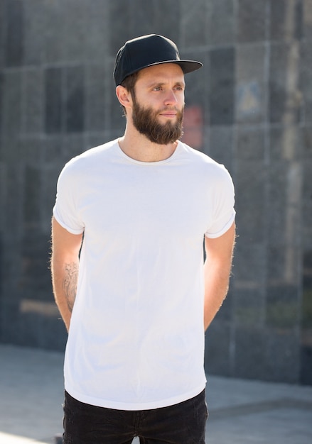 Hipster handsome male model with beard  wearing white blank  t-shirt with space for your logo or design in casual urban style