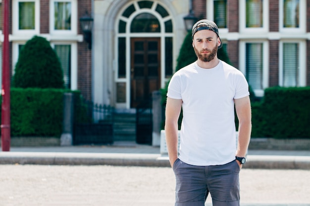 Hipster handsome male model with beard  wearing white blank  t-shirt with space for your logo or design in casual urban style