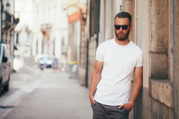 Hipster handsome male model with beard wearing white blank t-shirt with space for your logo or design in casual urban style