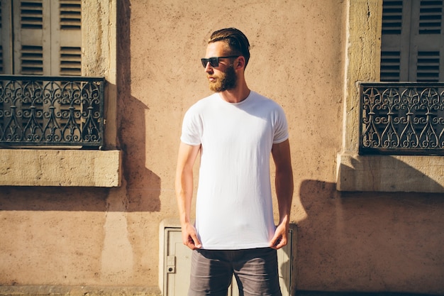 Hipster handsome male model with beard wearing white blank t-shirt with space for your logo or design in casual urban style