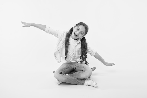 Hipster happy child pretend flying on penny board on yellow background Little girl dream of sky with arms outstretched like wings Enjoying skateboarding Carefree kid Freedom is free