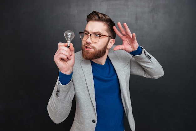 Hipster has idea. in studio. looking at bulb. isolated black surface