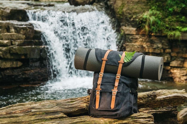 Hipster hiker tourist backpack on background of the river and the waterfall