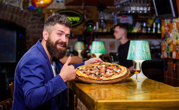 Hipster hungry eat italian pizza. Hipster client sit at bar counter. Man received delicious pizza. Enjoy your meal. Cheat meal concept. Pizza favorite restaurant food. Fresh hot pizza for dinner.