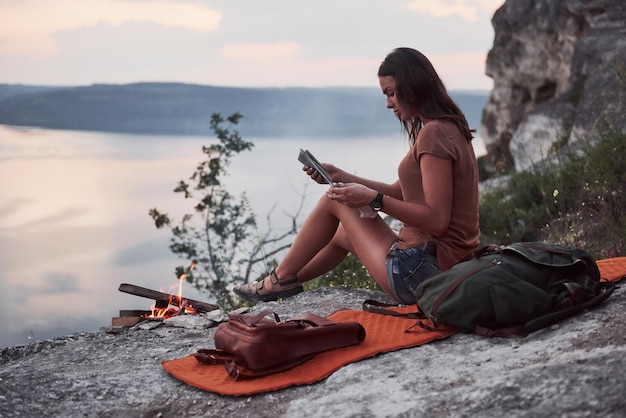 Hipster jong meisje die met rugzak van zonsondergang op piek van rotsberg genieten. Toeristische reiziger op achtergrond weergave mockup