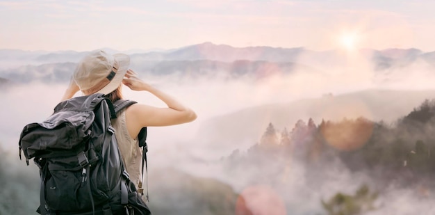 Hipster jong meisje met rugzak genieten van zonsondergang op de top van de mistige berg