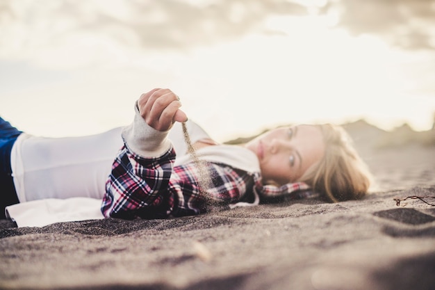 Hipster jong schattig blond kaukasisch meisje speelt met het zand op het strand