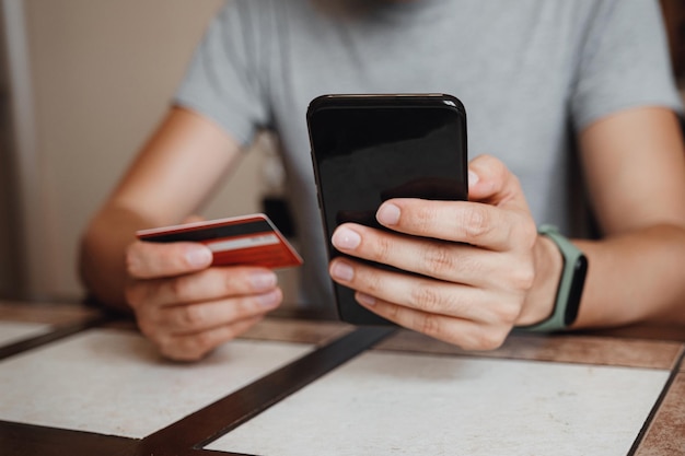 Hipster jonge man online winkelen met creditcard met behulp van slimme telefoon thuis