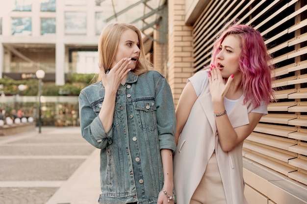 Hipster jonge volwassen vrienden omarmen terwijl ze rondhangen in de stad. Twee jonge vrouwen die lachen en lopen en genieten van een zorgeloze vakantielevensstijl