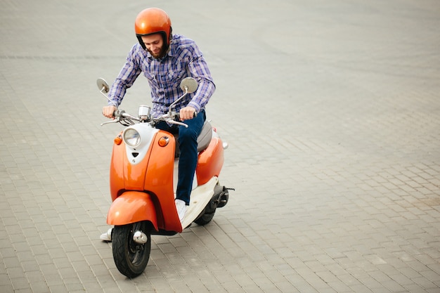 Hipster jongeman in helm rijdt op gele retro scooter in de stad