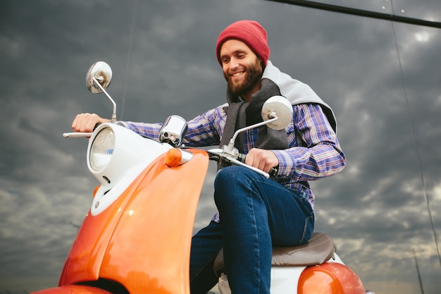 Hipster jongeman in helm rijdt op gele retro scooter in de stad