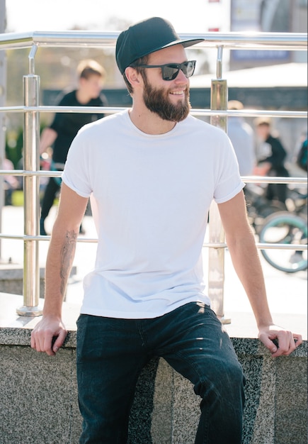 Hipster knap mannelijk model met baard, gekleed in een wit leeg t-shirt met ruimte voor uw logo of ontwerp in casual stedelijke stijl