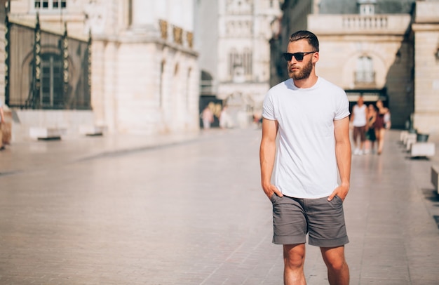 Hipster knap mannelijk model met baard, gekleed in een wit leeg t-shirt met ruimte voor uw logo of ontwerp in casual stedelijke stijl