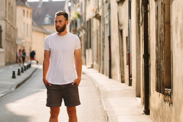 Hipster knap mannelijk model met baard, gekleed in een wit leeg t-shirt met ruimte voor uw logo of ontwerp in casual stedelijke stijl