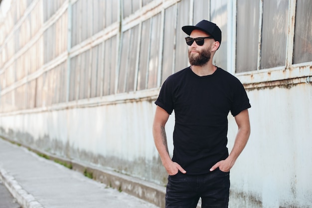 Hipster knap mannelijk model met baard, gekleed in een zwart leeg t-shirt met ruimte voor uw logo of ontwerp in een ongedwongen stedelijke stijl