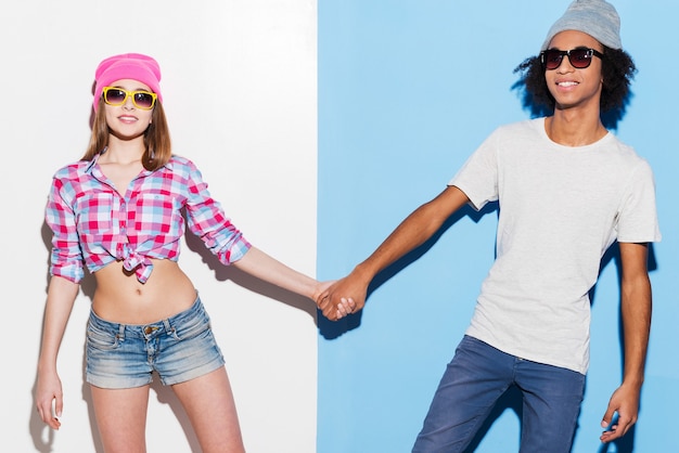 Hipster love. Funky young couple wearing sunglasses and smiling while standing against colorful background