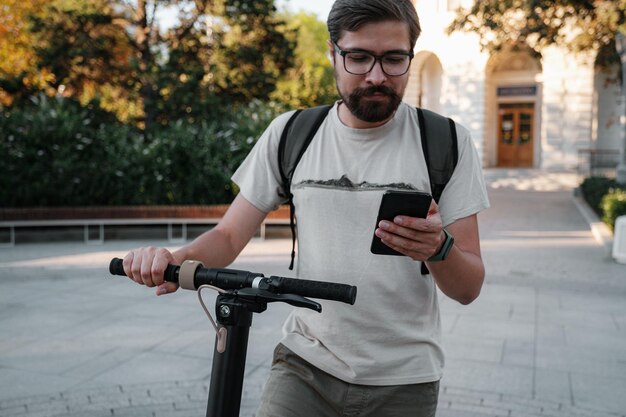 Foto hipster man forens met elektrische scooter buiten in de stad met smartphone