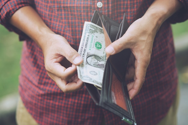 Mani dell'uomo hipster che tengono portafoglio con carte di credito e pila di soldi