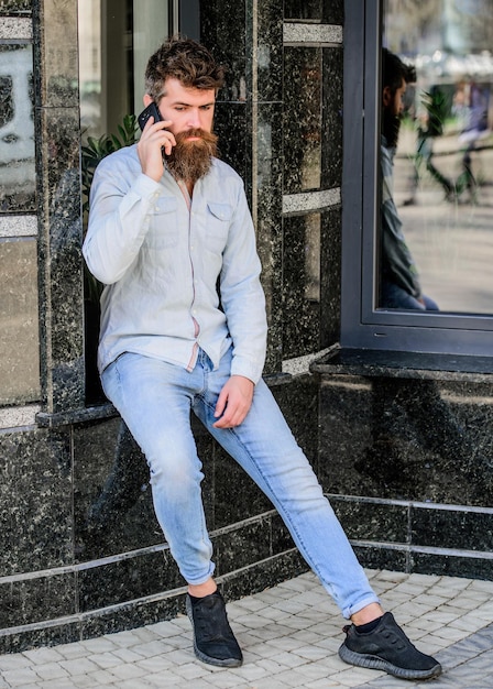 Hipster man houdt smartphone brute zakenman met mobiele telefoon bebaarde man spreken op mobiele telefoon gesprek en discussie volwassen hipster met baard zakelijke praten stedelijke mode-stijl