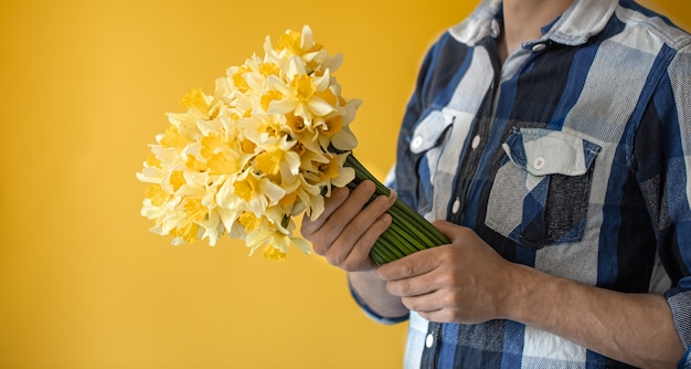 Hipster man op een gele muur in een shirt en een boeket bloemen.