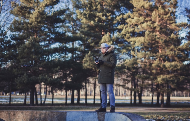 Хипстерский человек пилотирует дрон в парке. Парень тестирует беспилотный летательный аппарат на природе.