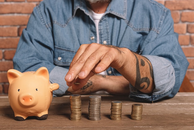 Hipster man stapelt munten met een spaarvarken varken op tafel om geld en financieel concept te besparen.