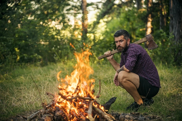 Hipster man with axe look at campfire flame