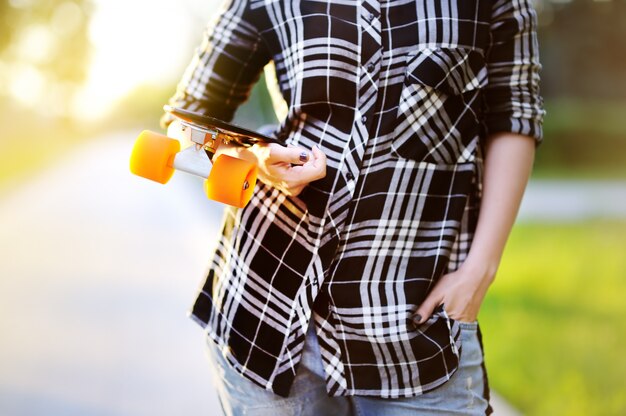 Hipster meisje met skateboard buitenshuis. close-upskateboard in vrouwelijke hand. actieve sportieve vrouw plezier in park