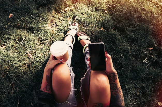 hipster meisje zit in park met smartphone en koffie