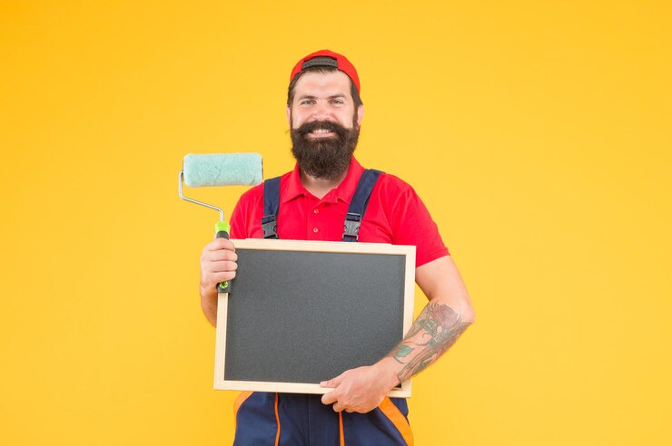 Foto hipster met kopieerruimte aan boord van reparatie en bouwvakman op constructie creativiteit wederopbouw reclame bebaarde man met verfroller en schoolbordschilder bij schilderwerken