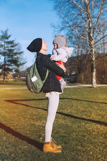 Hipster mother with her baby dressed in warm clothes walking on a sunny day outdoors