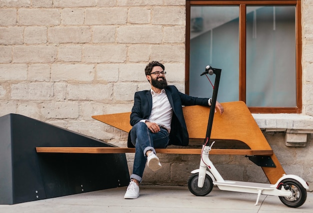 Hipster ontspannen in de buurt van elektrische scooter op de bank