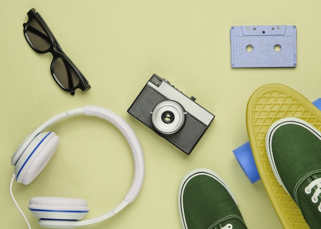 Hipster-outfit. Skateboard met koptelefoon, audiocassette, retro camera en sneakers op groene pastelachtergrond. Creatief modeminimalisme. Minimaal zomerplezier. Bovenaanzicht