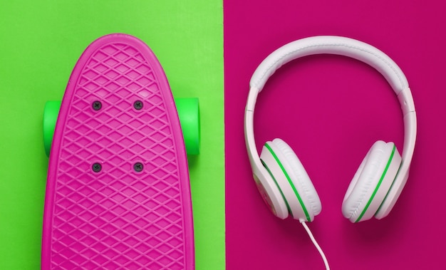 Hipster outfit. Skateboard with headphones on colored background. Creative fashion minimalism. Trendy old fashionable style. Minimal summer fun. Music concept. Top view