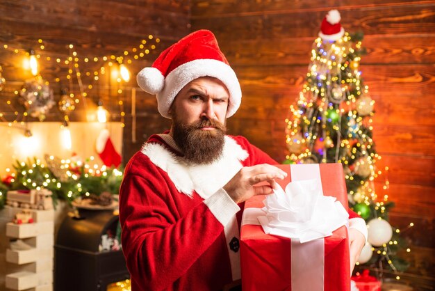 Hipster in red santa hat holding present styling santa hipster with a long beard posing on the chris...