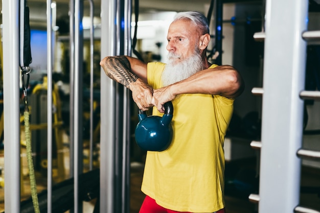 写真 ジム内でトレーニングする流行に敏感な年配の男性-ケトルベルを持っている手に焦点を当てる