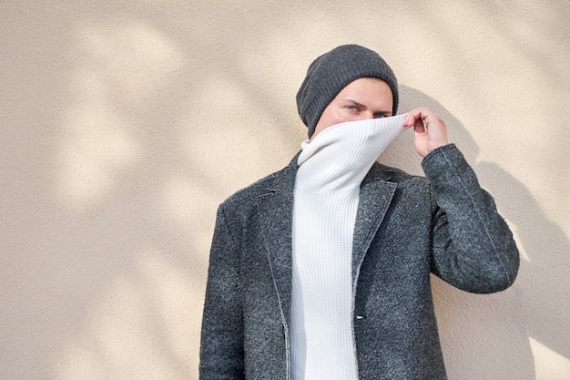 Foto hipster stijlvolle man met een modieuze grijze jas gezicht met witte trui verbergen.