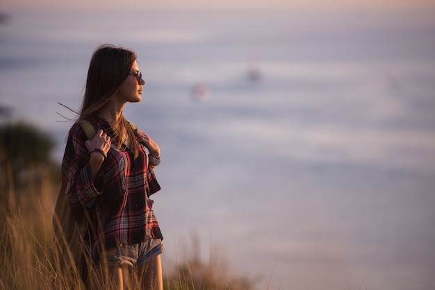 Hipster stylish woman traveler looking at a sea at sunset