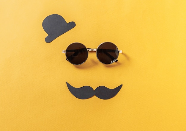 Hipster sunglasses and funny moustache with hat on yellow 