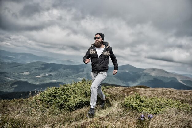 Hipster voelt zich vrij tijdens het wandelen op de hemelachtergrond Hipster of brutale macho verovert berg Man met brutaal uiterlijk wandelen Vrijheidsconcept Man met baard geniet van vrijheid loopt op de top van de berg