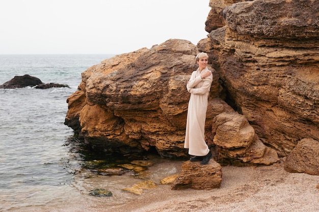 Hipster vrouw in de buurt van zee en rotsen Vrouwelijk model met kort haar dat op een bewolkte dag loopt Natuur vrije tijd concept