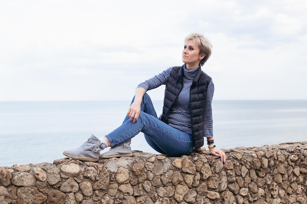 Hipster vrouw zittend op de stenen stoep in de buurt van zee in de herfst