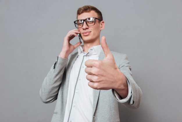 Hipster with phone showing finger up isolated on gray