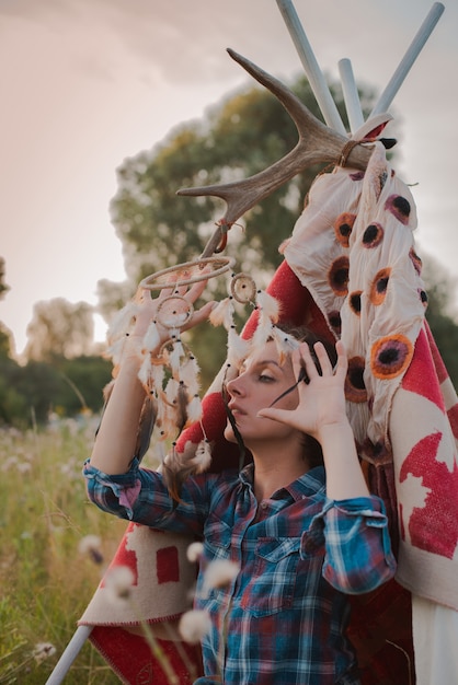 Photo hipster woman in the form of a shaman is looking for inspiration from mother earth in a wigwam in nature.