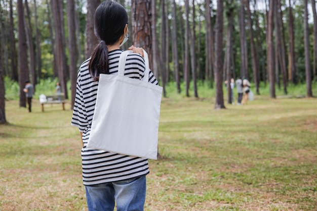 Hipster woman holding white cotton bag at park